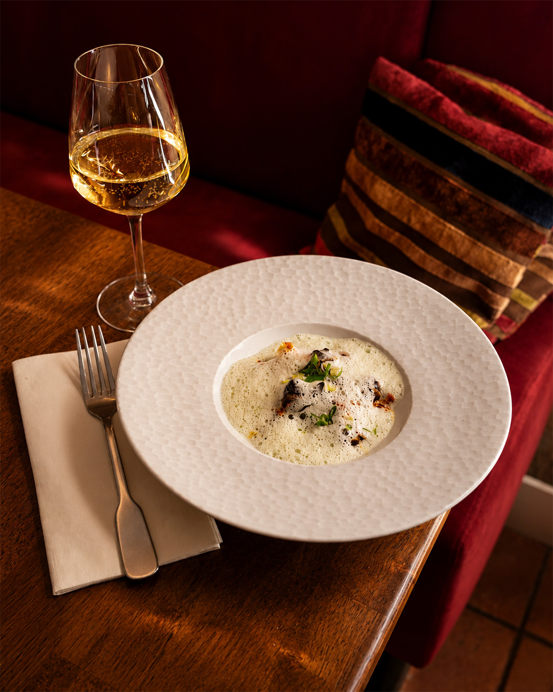 Assiette creuse blanche avec une écume légère, verre de vin blanc et banquette rouge